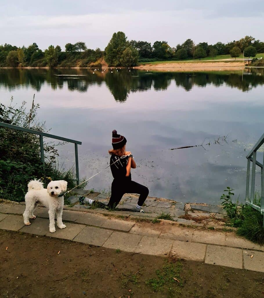 Junges Mädchen joggt mit ihrem Hund am Ufer des Rotter Sees in Troisdorf, umgeben von ruhiger Natur.