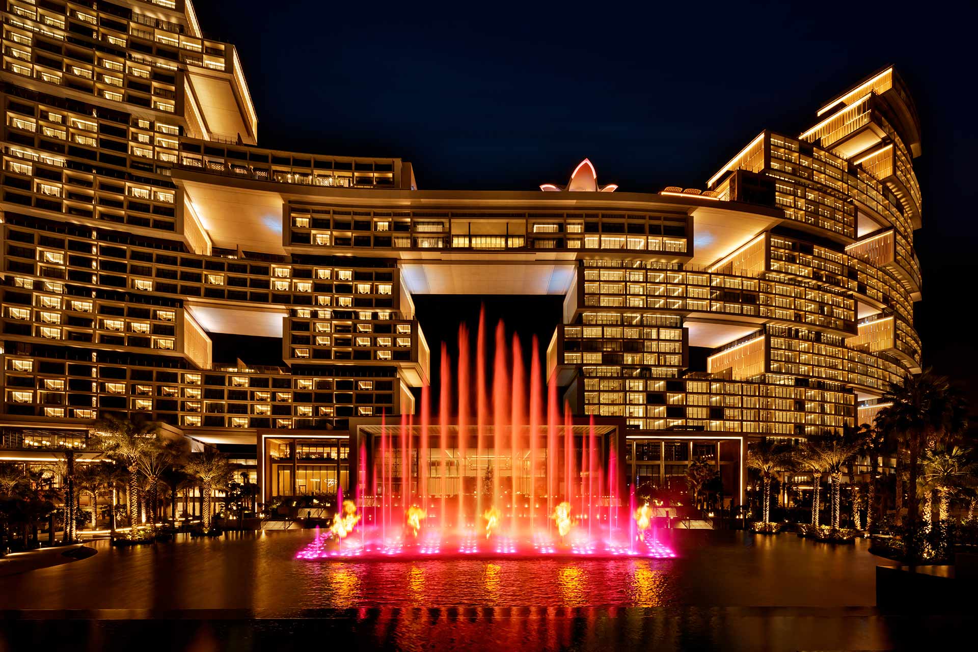 Das Foto zeigt das Atlantis The Royal Hotel in Dubai bei Nacht, mit beleuchteten Fassaden und der Skyblaze Fountain im Vordergrund.