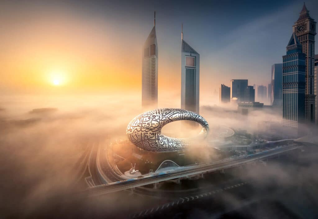 Das Foto zeigt ein atemberaubendes Bild von Dubais Museum der Zukunft, umgeben von Hochhäusern im Morgennebel, aufgenommen bei Sonnenaufgang.