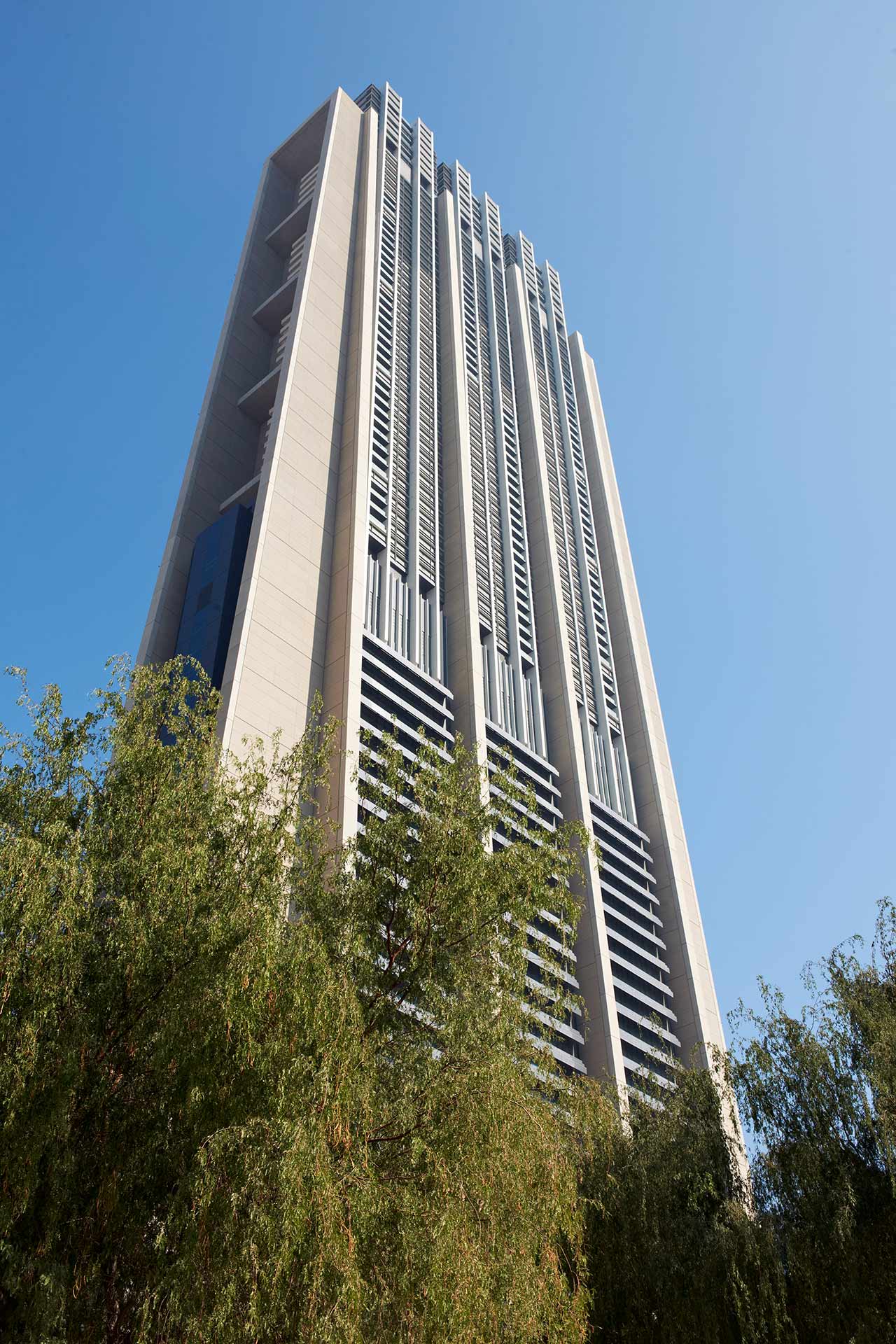 Das Foto zeigt den Index Tower in Dubai, ein modernes Hochhaus entworfen von Foster + Partners, mit grünem Laub im Vordergrund.
